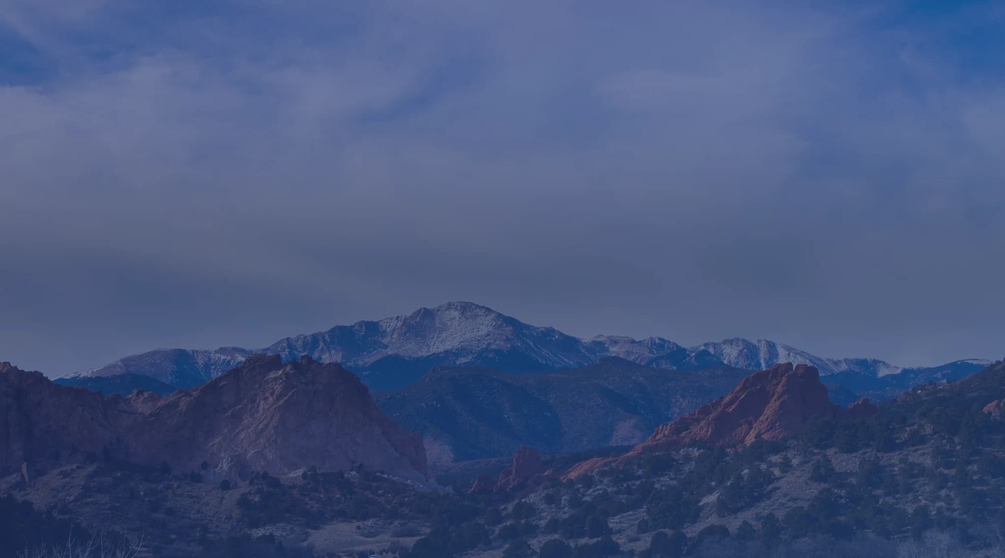 Red sandstone formations at Garden of the Gods with snow-capped Pikes Peak behind them near Colorado Springs