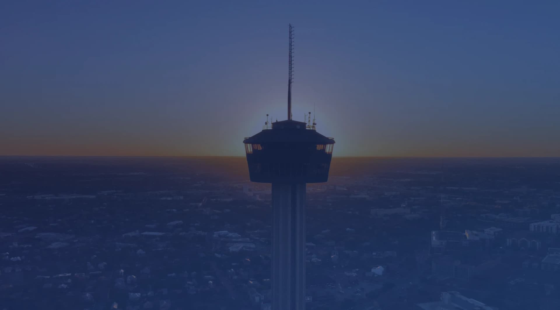 Silhouette of the Tower of the Americas against a sunset over San Antonio, Texas