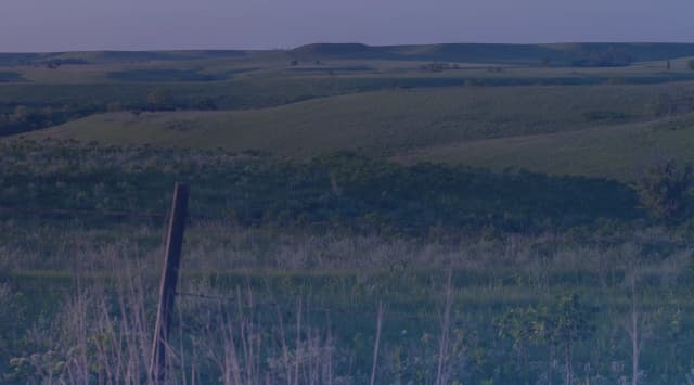 Rolling green Flint Hills prairie in Kansas with a weathered wooden fence post in the foreground