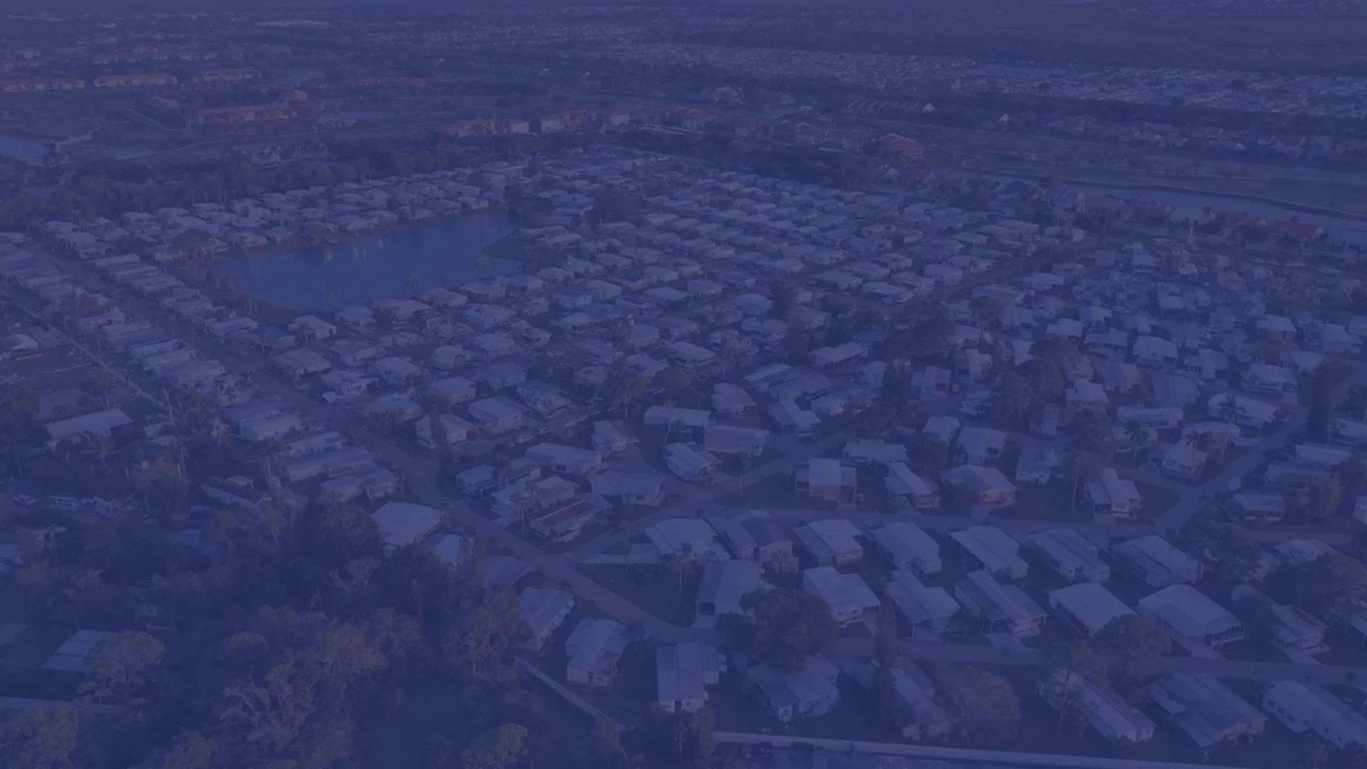 Aerial view of a Jacksonville-area residential neighborhood at dusk with rooftops, a small lake, and palms stretching to the horizon.