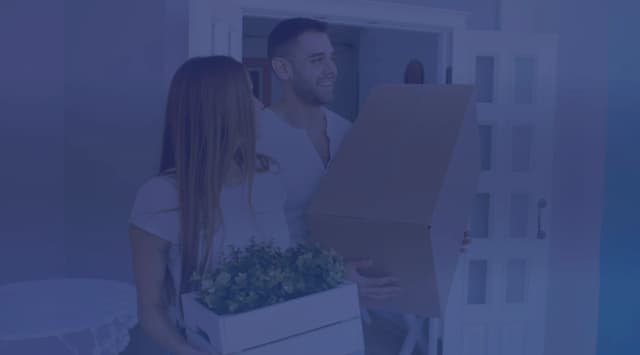 A couple carrying moving boxes through the front door of a new home