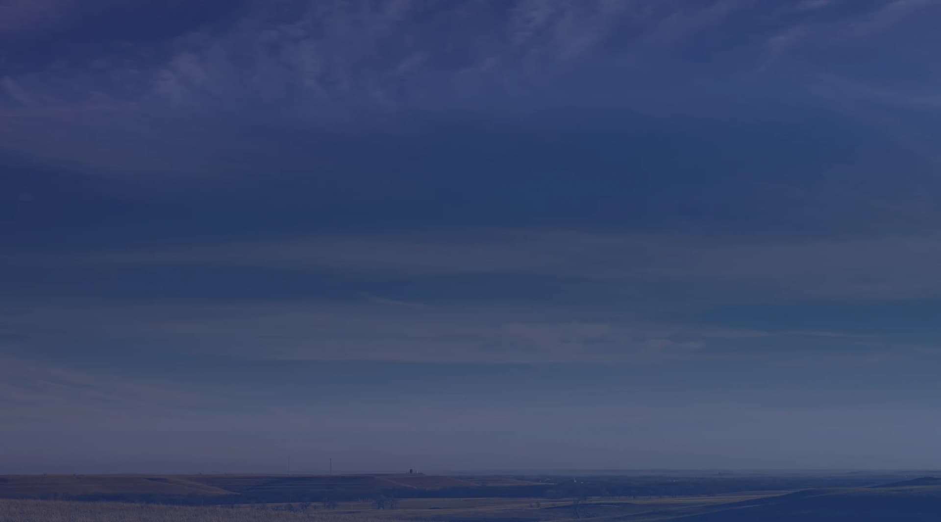 Rolling golden grassland stretches toward a low horizon under a broad blue sky streaked with wispy clouds.