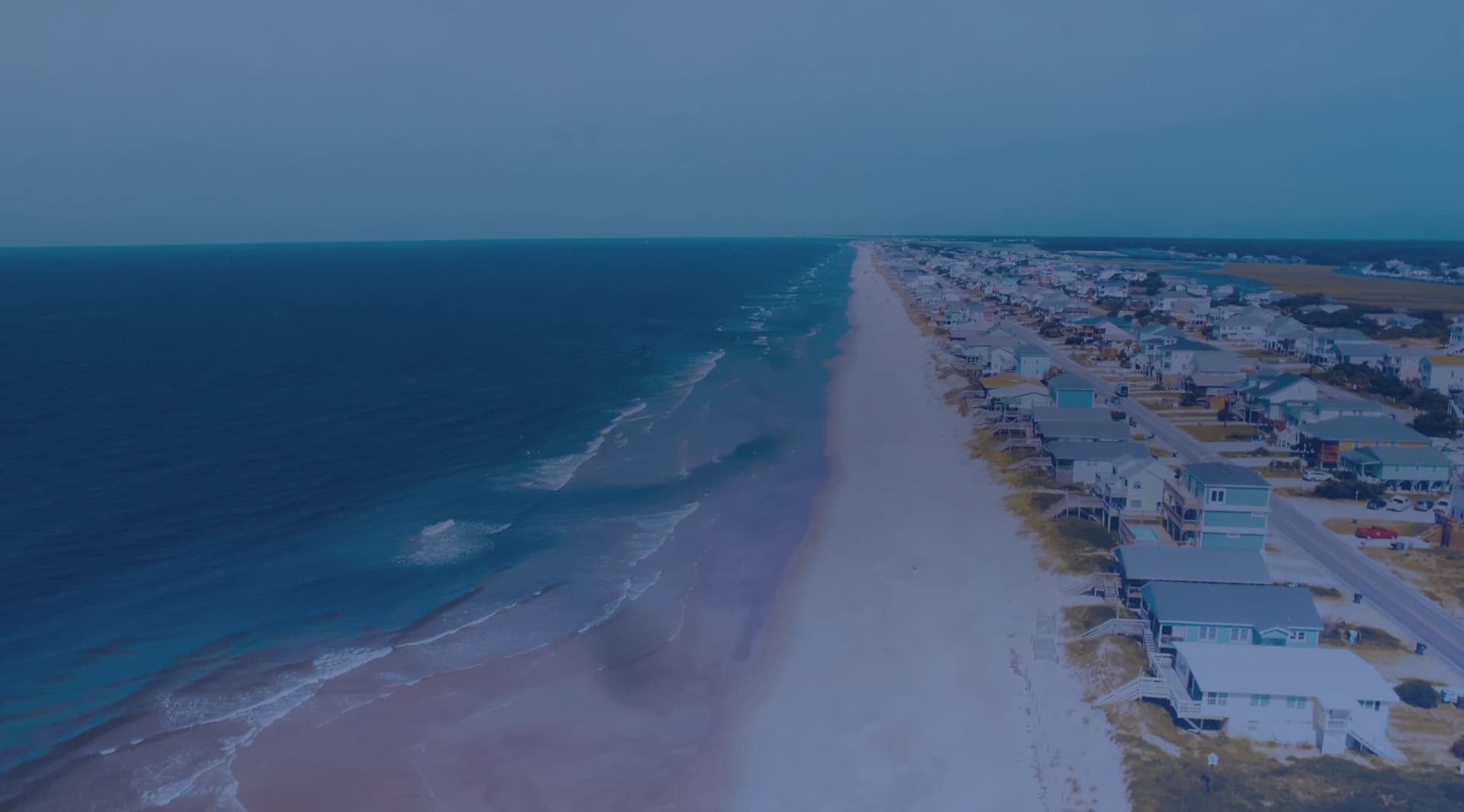 Aerial view of a North Carolina barrier island beach with waves rolling in beside a row of beach houses