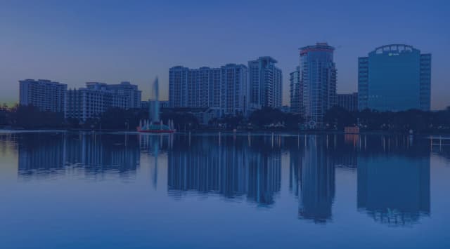The downtown Orlando skyline and the Lake Eola fountain reflected in calm water at sunrise.