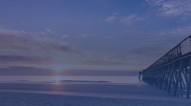 Sunrise over the Atlantic Ocean beside a long wooden fishing pier on a quiet beach