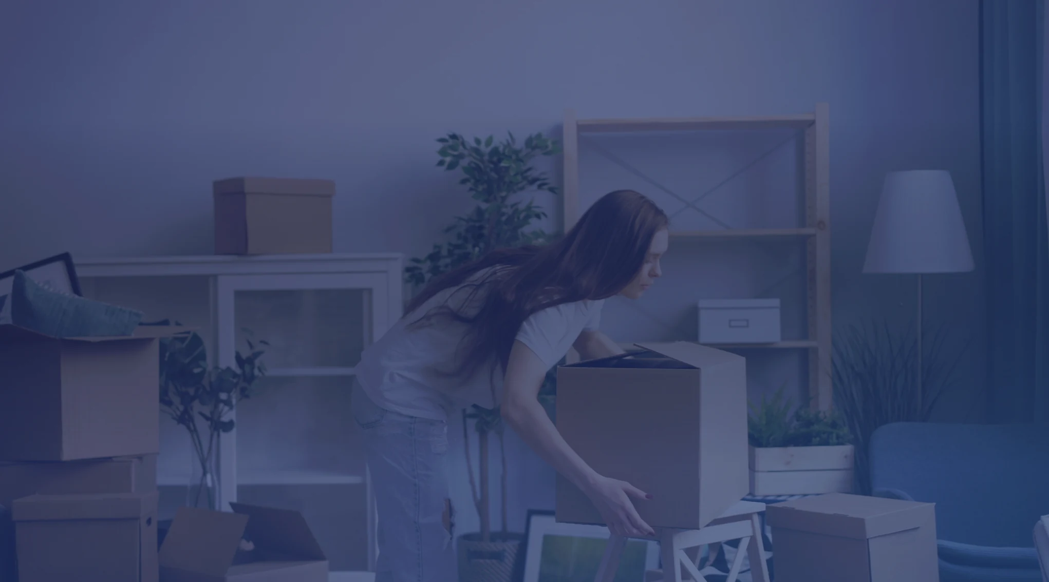 A woman lifting a moving box in a living room still full of packed boxes