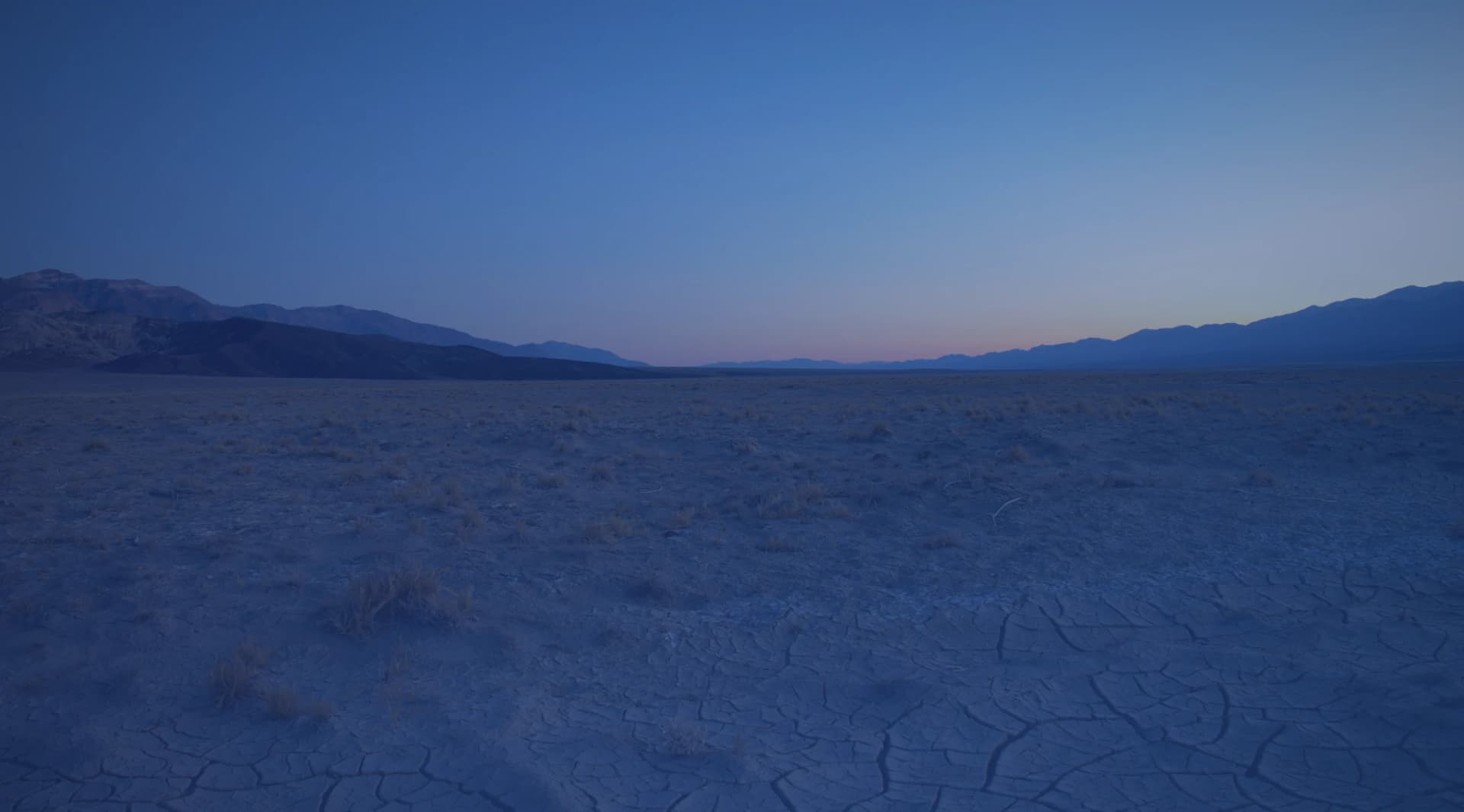 Open high desert scenery of sand, scrub, and distant mountains, like the Mojave Desert near Barstow, California.