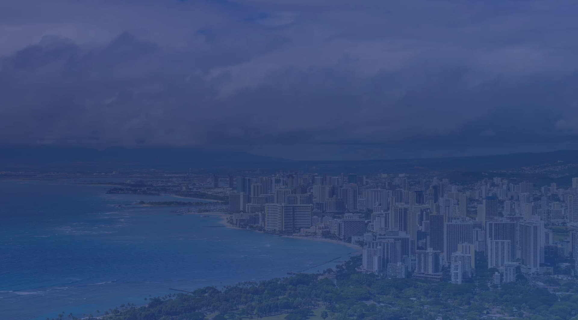 Aerial view of the Honolulu skyline and Waikiki Beach from Diamond Head, with turquoise ocean water and the Koolau Mountains in the background