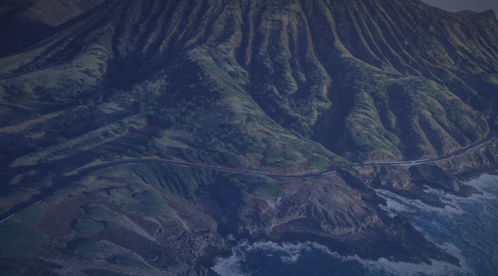 A green mountain ridge meeting the rocky Oahu coastline in Hawaii.
