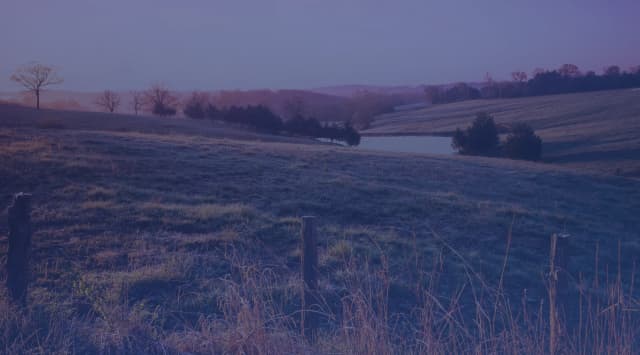 Rolling Missouri pastures at dawn, with a small pond, fence posts, and open farmland typical of the countryside near Whiteman Air Force Base