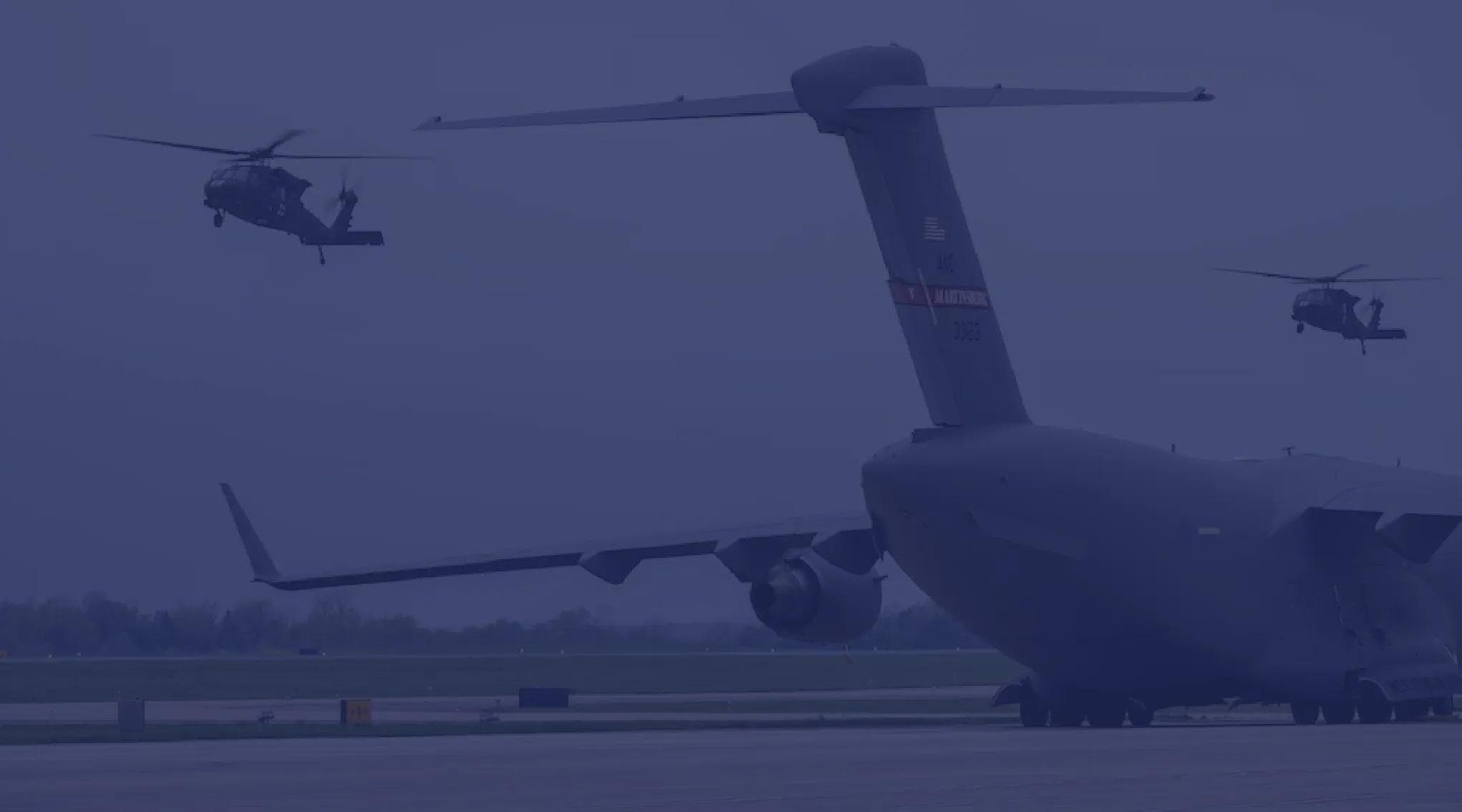 A C-5 Galaxy cargo plane sits on the runway in West Virginia while AH-64 Apaches fly around it.
