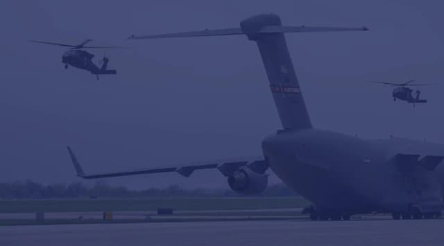 A C-5 Galaxy cargo plane sits on the runway in West Virginia while AH-64 Apaches fly around it.