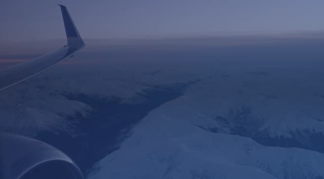 Snow-covered mountain ranges seen from an aircraft window, with the wing in the foreground