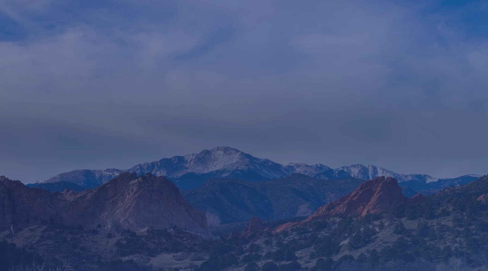 Red sandstone formations at Garden of the Gods with snow-capped Pikes Peak behind them near Colorado Springs