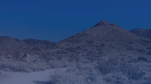 A rocky desert peak rising over sagebrush and a sandy trail under a clear New Mexico sky