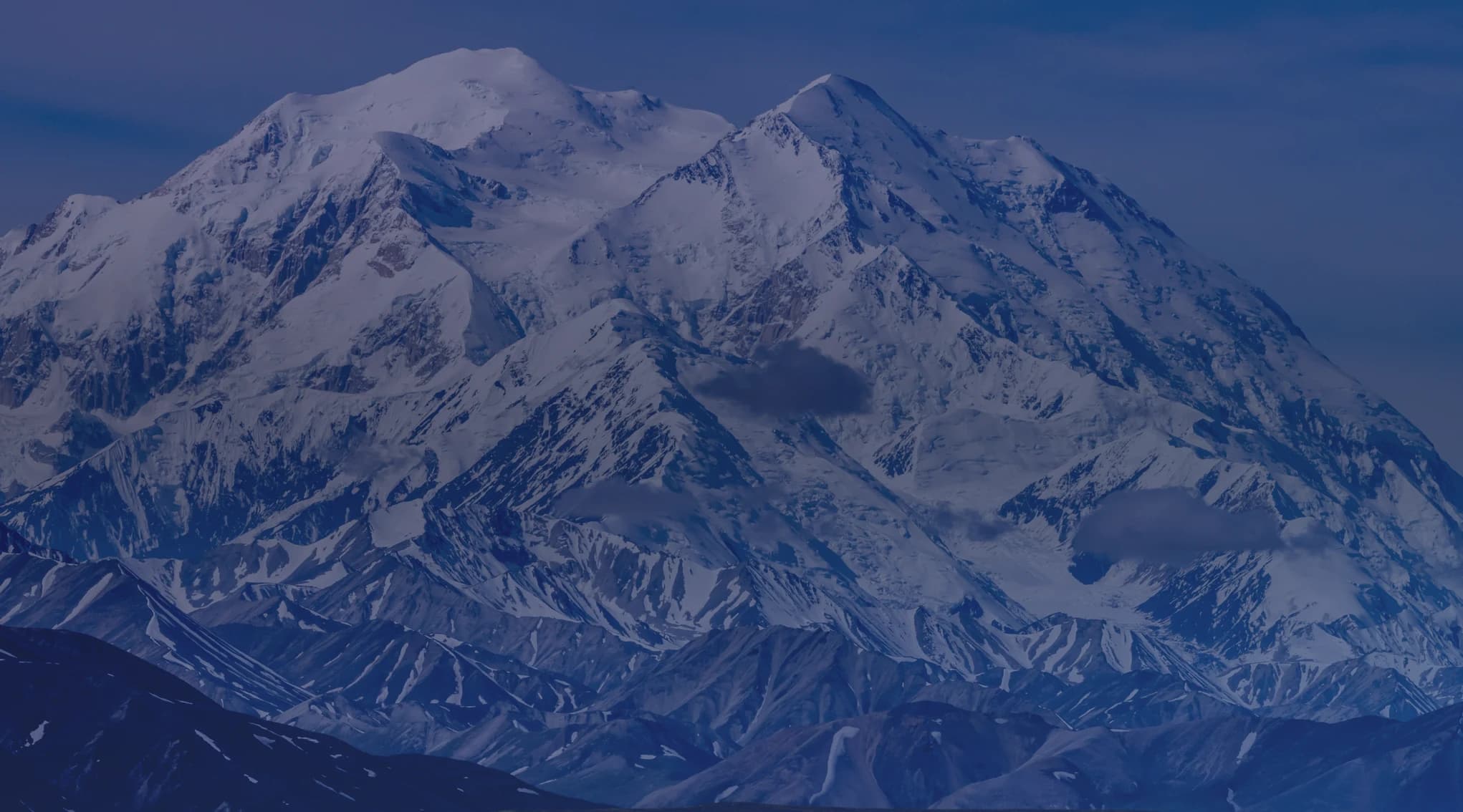 A snow-covered Alaska mountain range rising above lower ridgelines under a clear sky