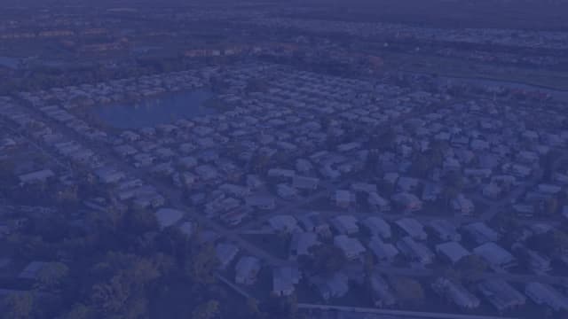 Aerial view of a Jacksonville-area residential neighborhood at dusk with rooftops, a small lake, and palms stretching to the horizon.