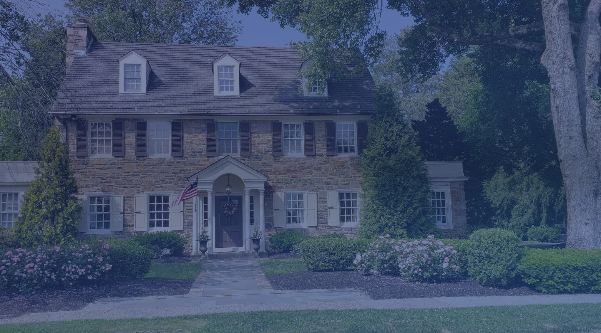 Two-story stone home with symmetrical windows on a tree-lined residential street