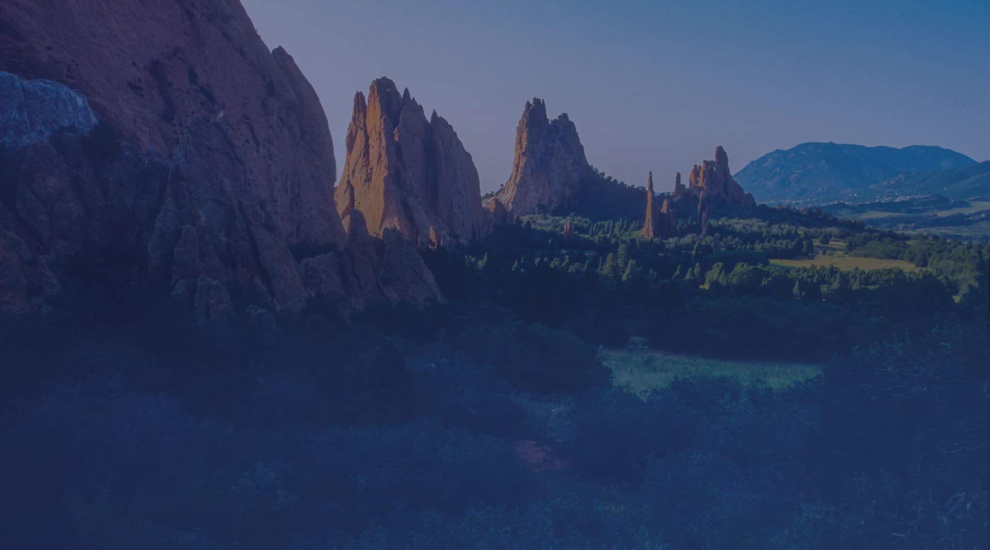 Red sandstone rock formations rising above green foothills near Colorado Springs, in the Garden of the Gods area.