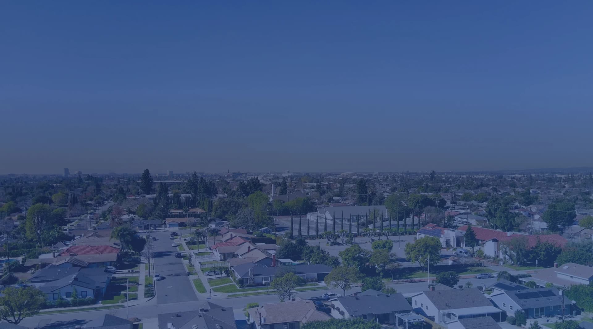 An aerial view of a suburban neighborhood with houses and trees under a clear sky