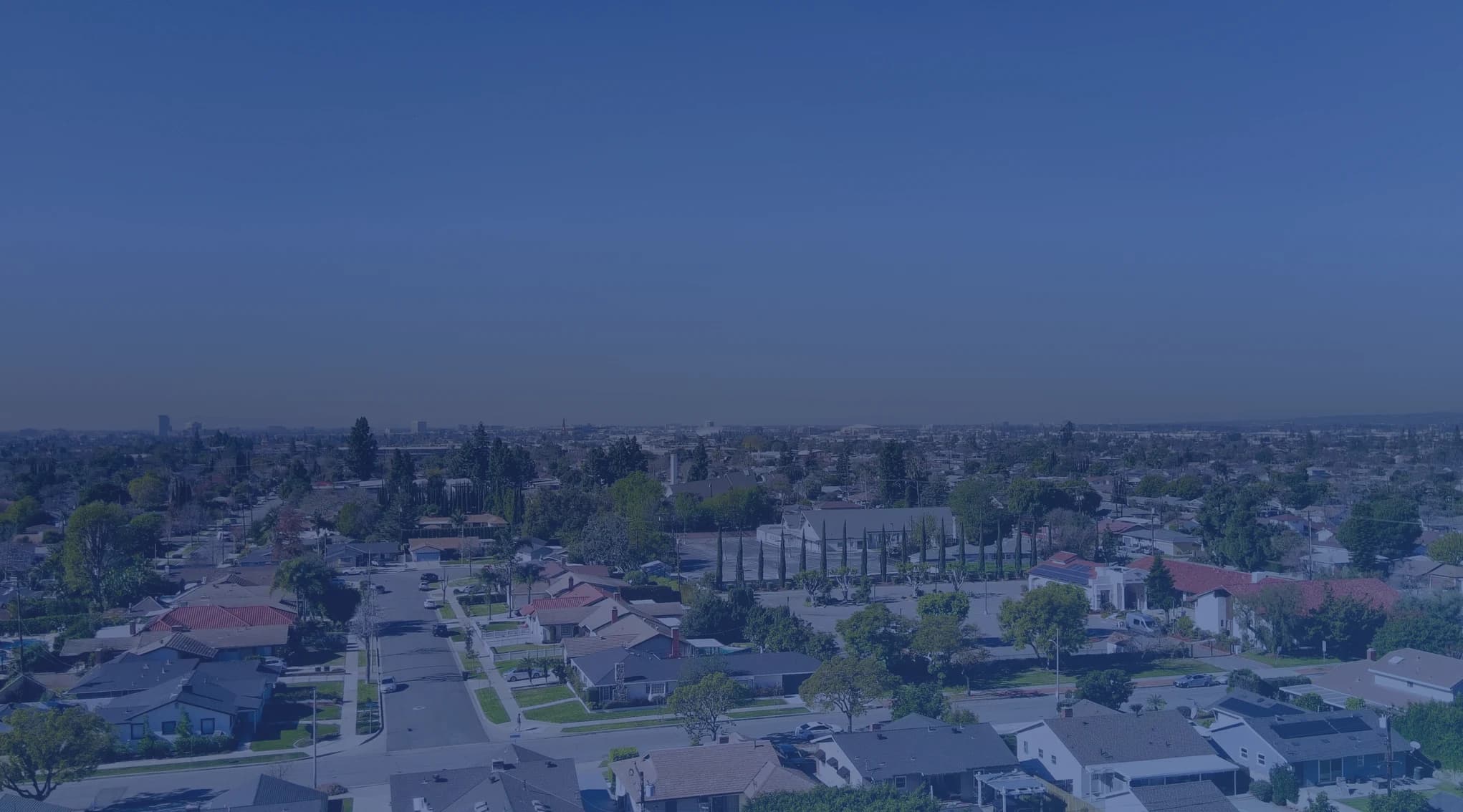 An aerial view of a suburban neighborhood with houses and trees under a clear sky