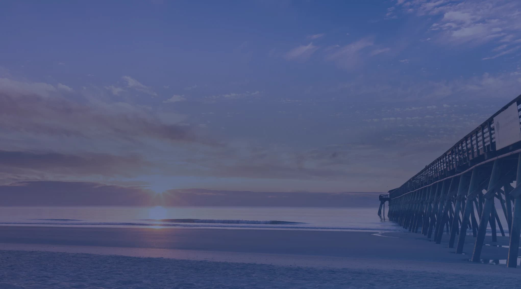 Sunrise over the Atlantic Ocean beside a long wooden fishing pier on a quiet beach