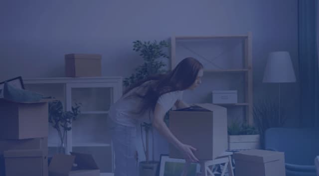 A woman lifting a moving box in a living room still full of packed boxes