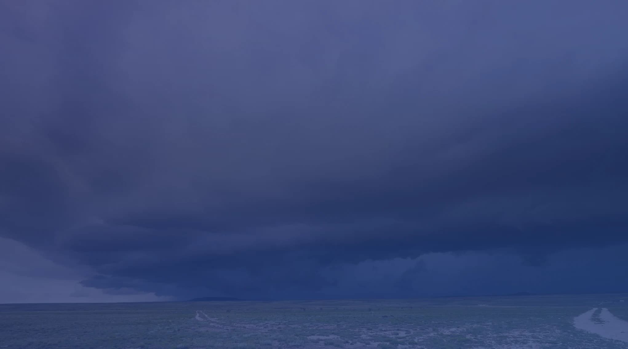 A shelf cloud advancing across the wide, open sky above the eastern New Mexico high plains, with a gravel road stretching toward the horizon