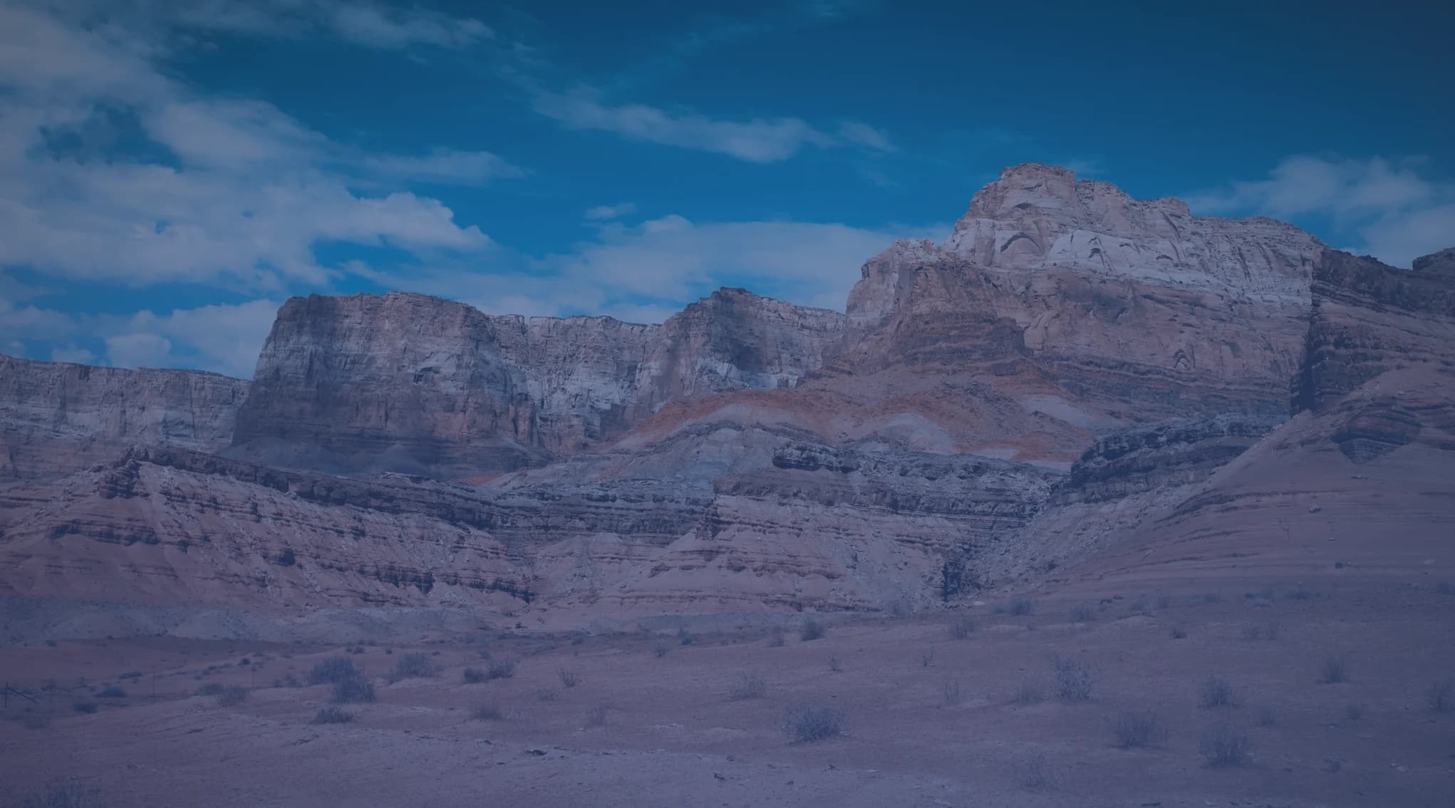 Red-rock cliffs rising above open high desert under a blue sky in the American Southwest.