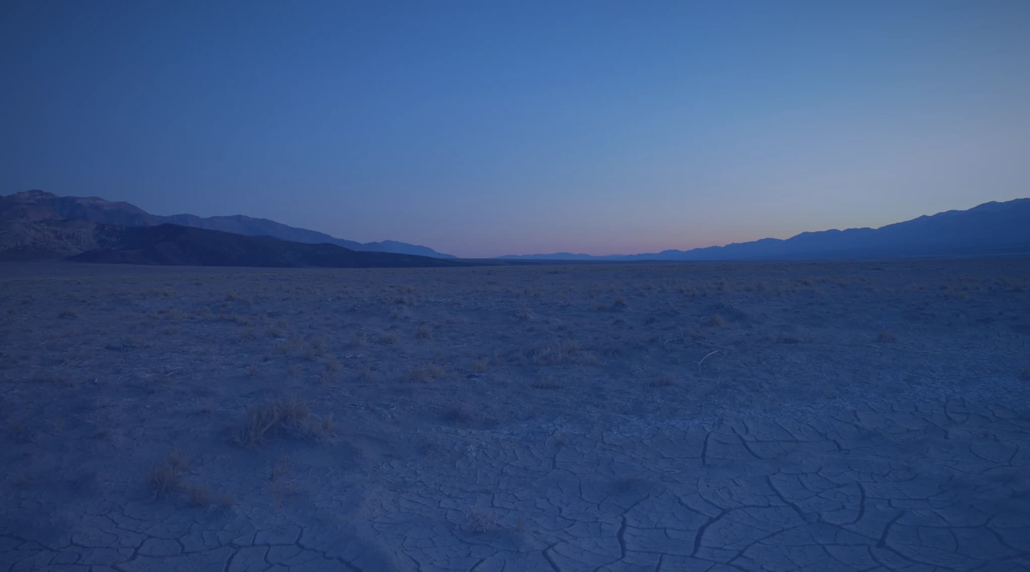 Open high desert scenery of sand, scrub, and distant mountains, like the Mojave Desert near Barstow, California.
