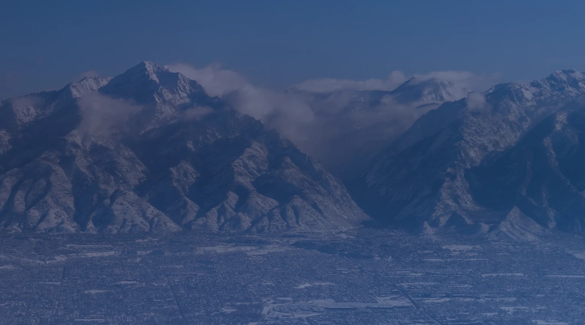 Aerial view of snow-covered Wasatch Mountains rising above the city grid of the Ogden and Salt Lake valley, Utah