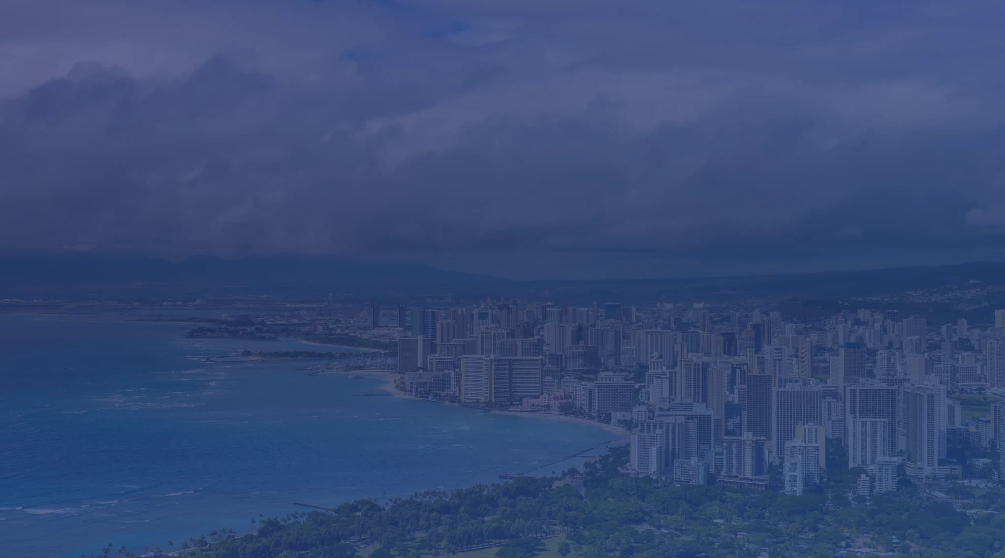 Aerial view of the Honolulu skyline and Waikiki Beach from Diamond Head, with turquoise ocean water and the Koolau Mountains in the background