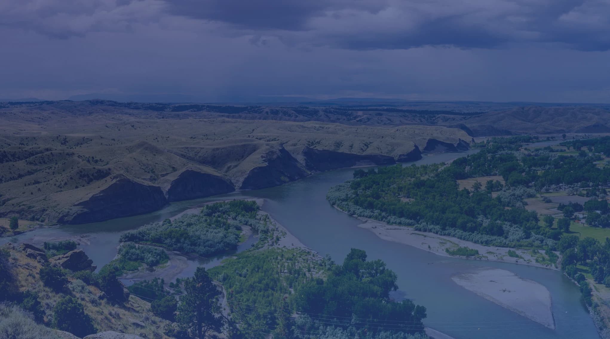 The Missouri River winding through the open plains and canyon country near Great Falls, Montana, under a wide, stormy sky