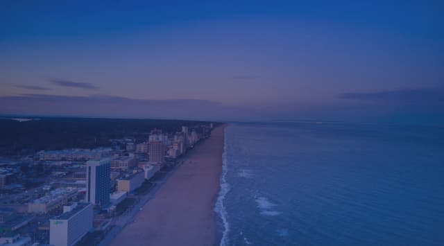 Virginia Beach oceanfront skyline at golden hour, with the Atlantic Ocean stretching to the horizon and the coastal boardwalk below