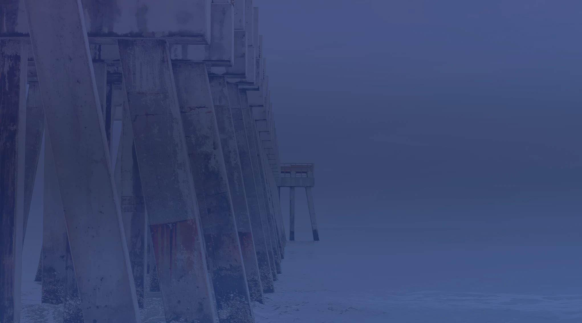 The Jacksonville Beach pier extending into the grey Atlantic Ocean, viewed from the sand on an overcast day