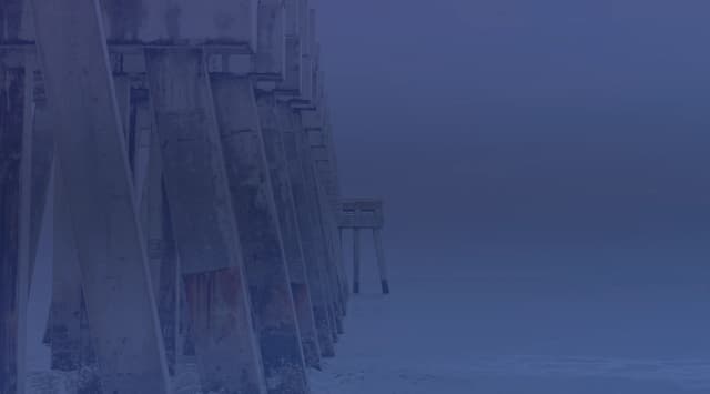 The Jacksonville Beach pier extending into the grey Atlantic Ocean, viewed from the sand on an overcast day