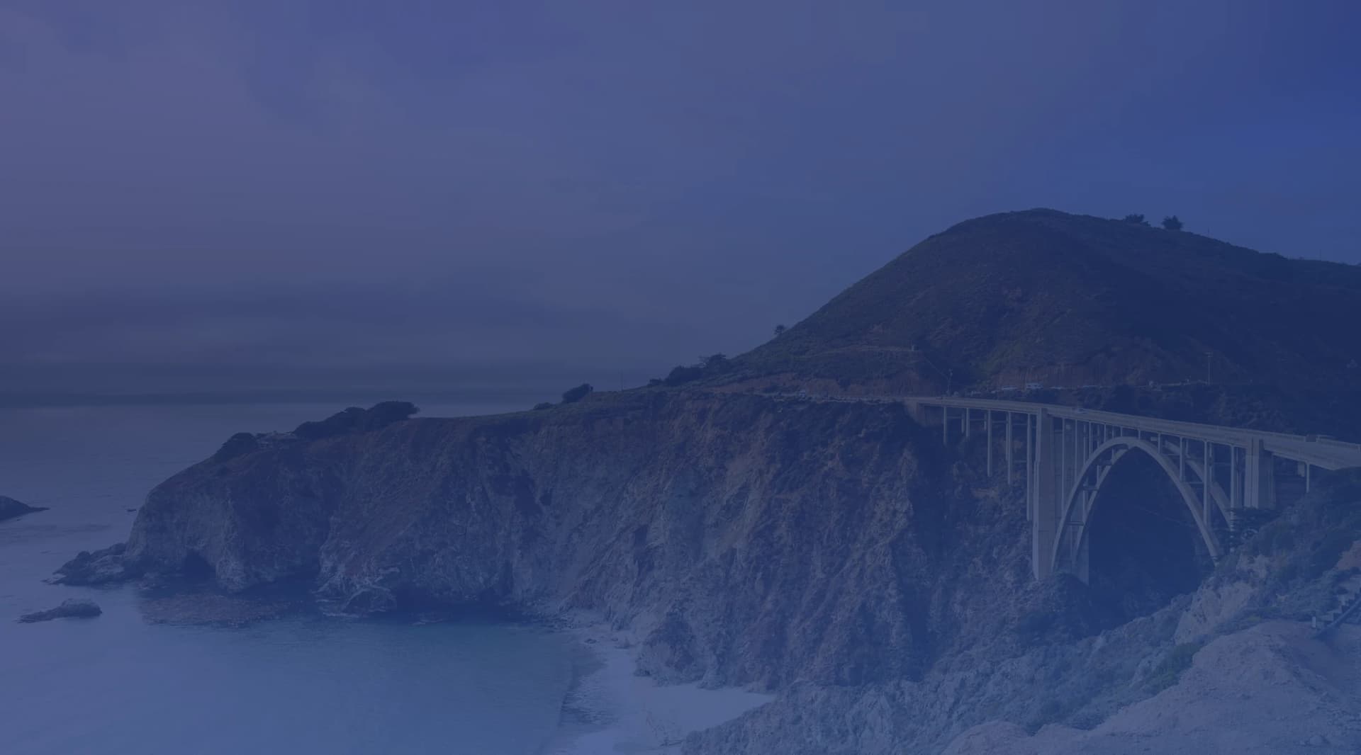 Bixby Creek Bridge arching over the Big Sur coastline with dramatic cliffs and the Pacific Ocean below, near Monterey, California