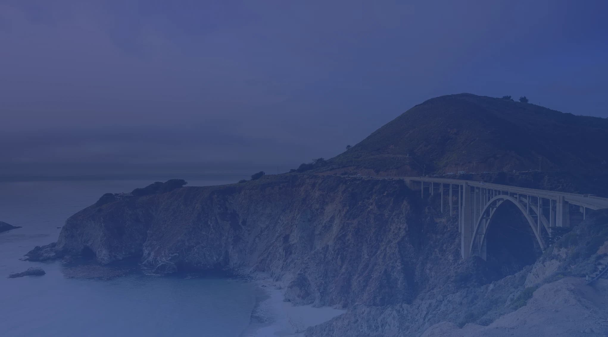 Bixby Creek Bridge arching over the Big Sur coastline with dramatic cliffs and the Pacific Ocean below, near Monterey, California