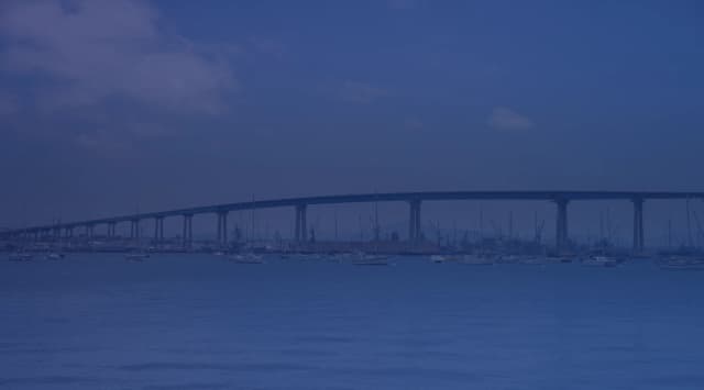 The Coronado Bridge spanning San Diego Bay with sailboats in the foreground and a bright blue sky above