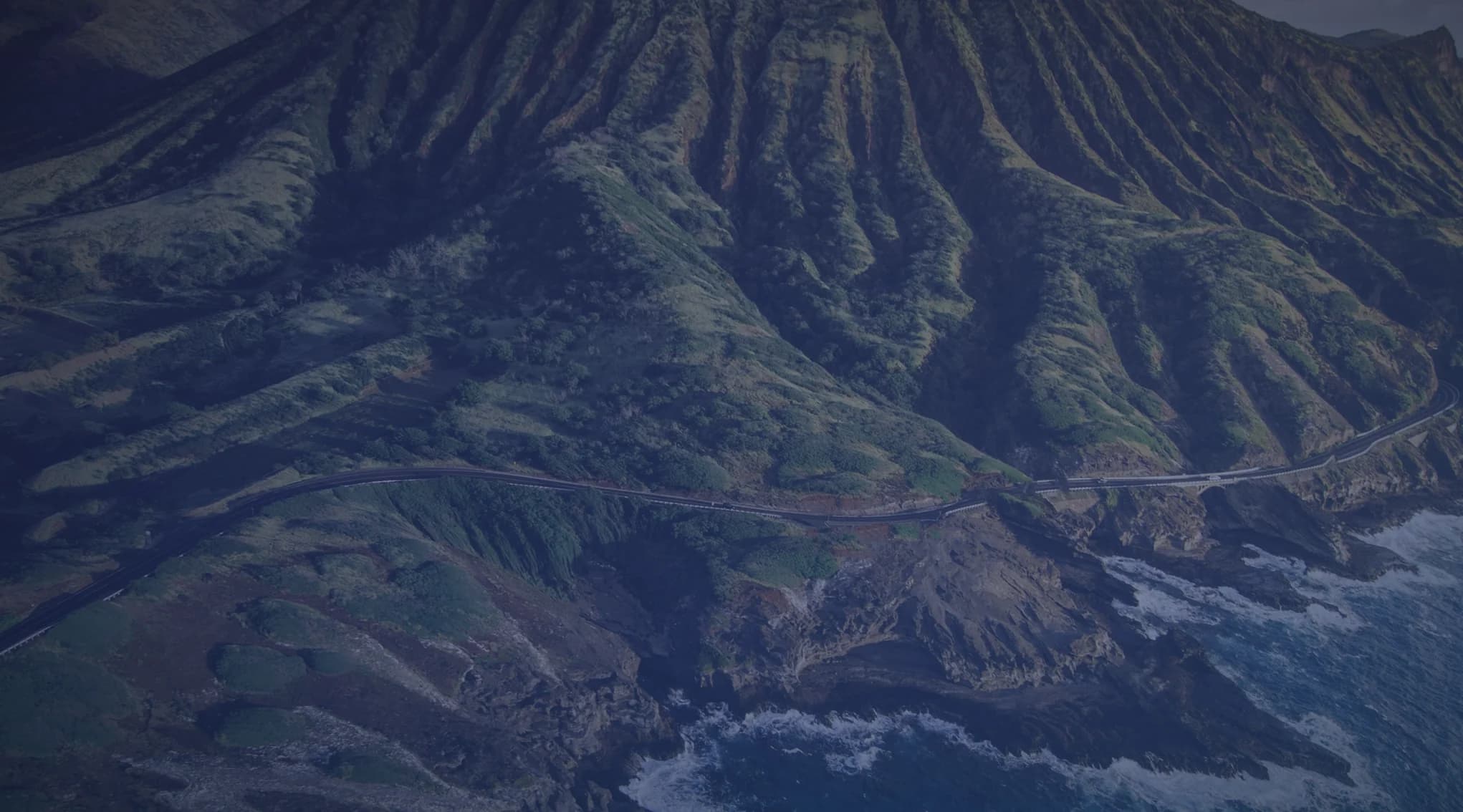 A green mountain ridge meeting the rocky Oahu coastline in Hawaii.