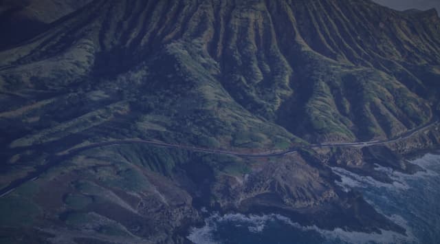 A green mountain ridge meeting the rocky Oahu coastline in Hawaii.