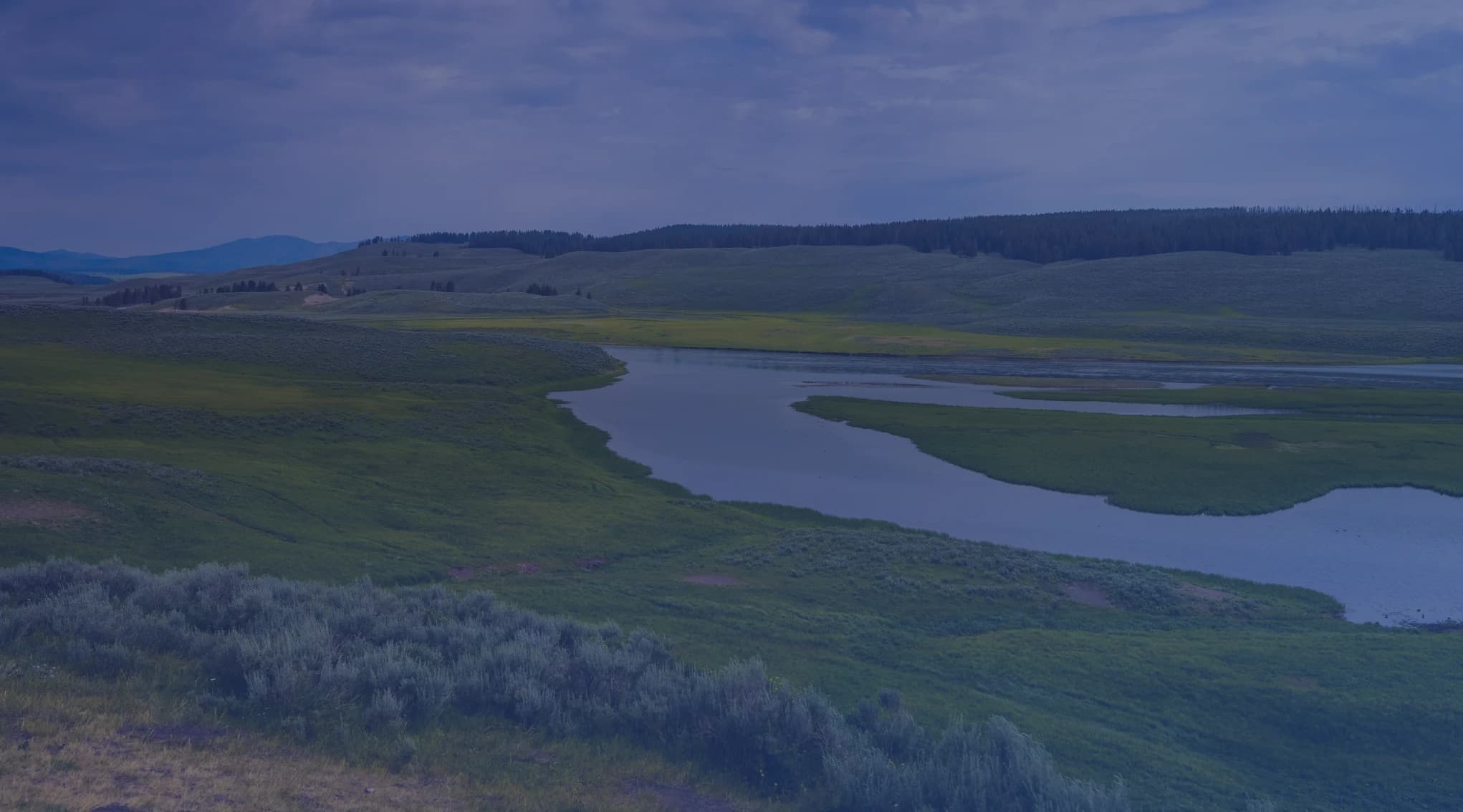 A river winding through a broad green valley under a cloudy summer sky.