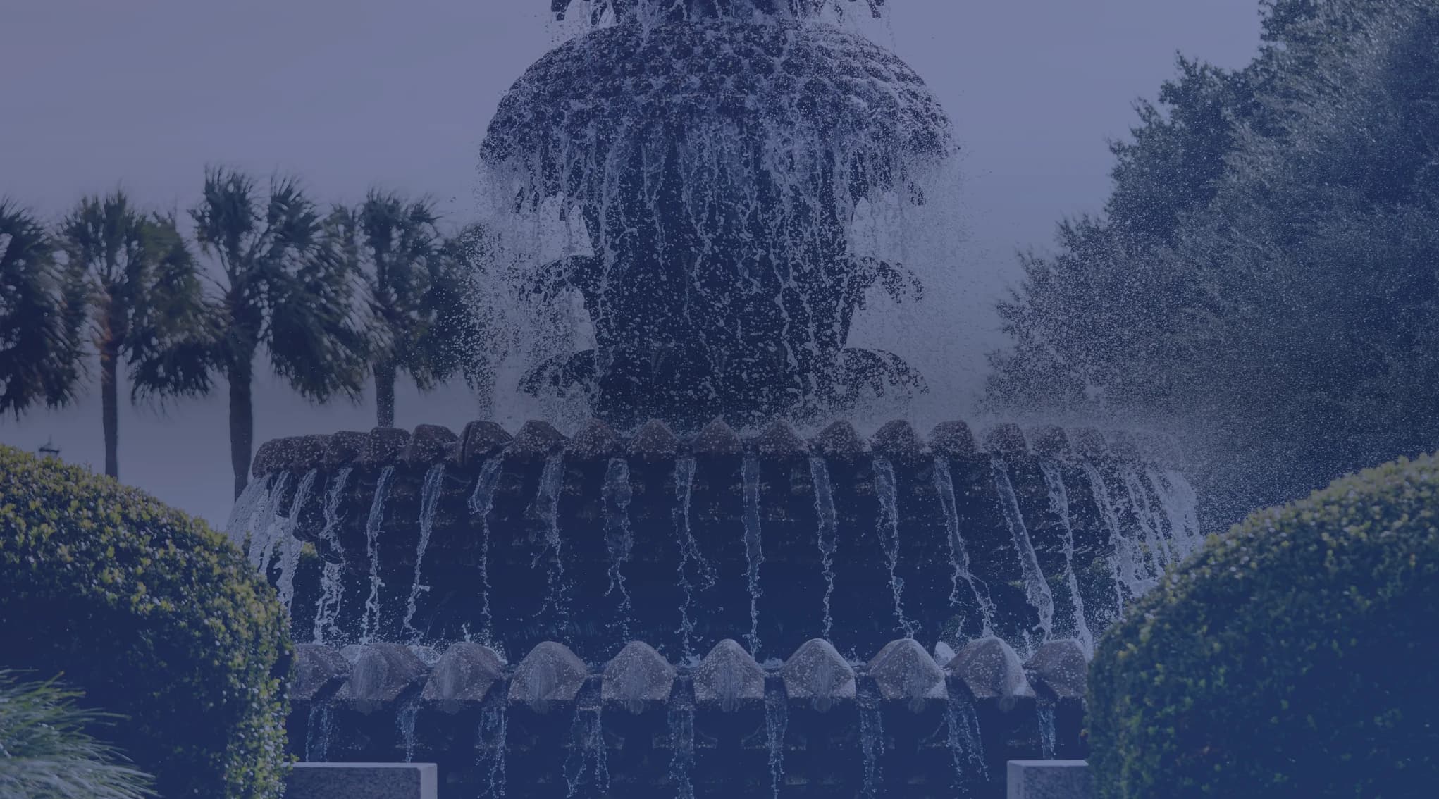 The pineapple fountain at Charleston's Waterfront Park, framed by palmetto trees and clipped hedges.
