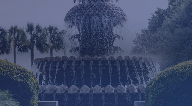 The pineapple fountain at Charleston's Waterfront Park, framed by palmetto trees and clipped hedges.