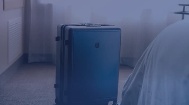 A packed suitcase standing beside a bed in a temporary lodging room