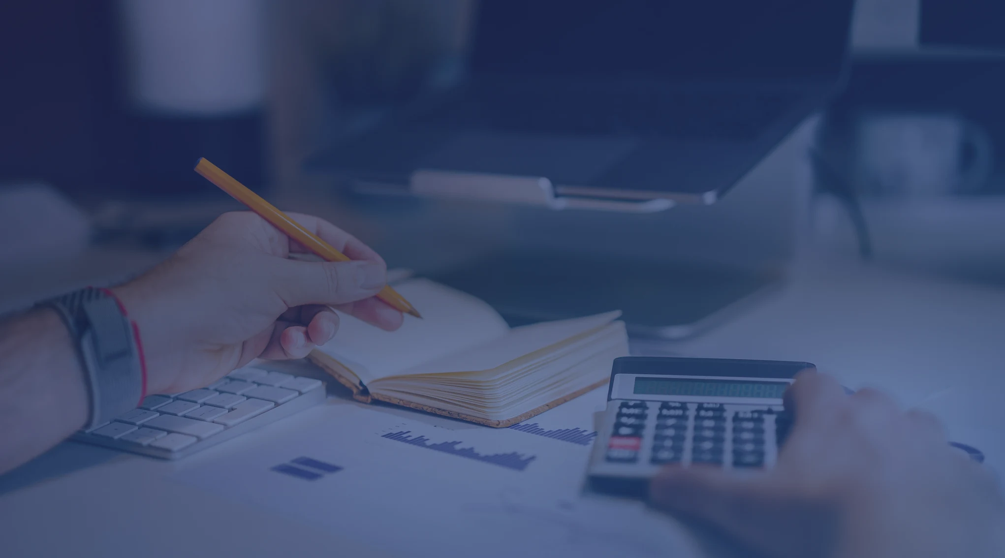 Hands with a pencil, notebook, and calculator reviewing finances at a desk