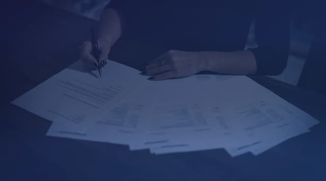 A woman seated at a table reviewing and signing a stack of documents
