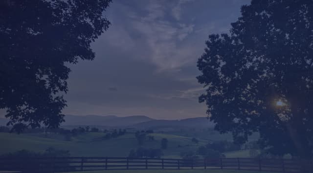 Rolling Shenandoah Valley farmland behind a wooden fence in Virginia, framed by trees at dusk.